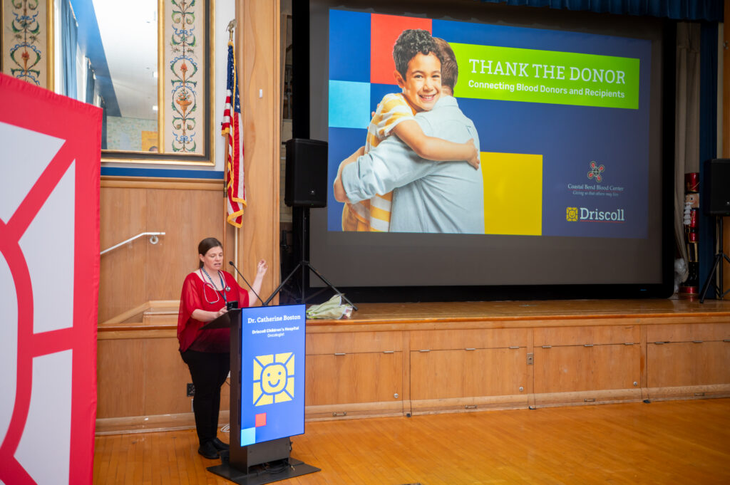 Oncologist stands in front of podium in auditorium during event at Driscoll.