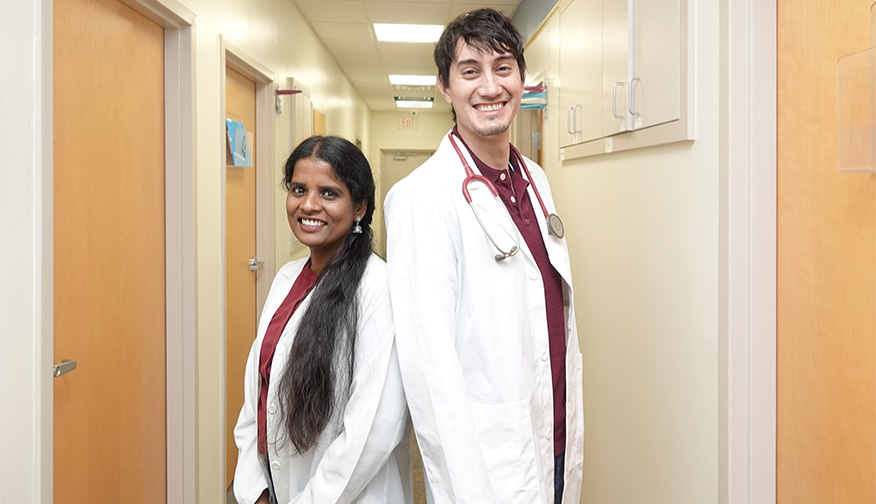 Smiling female and male doctors back to back in a hospital hallway.