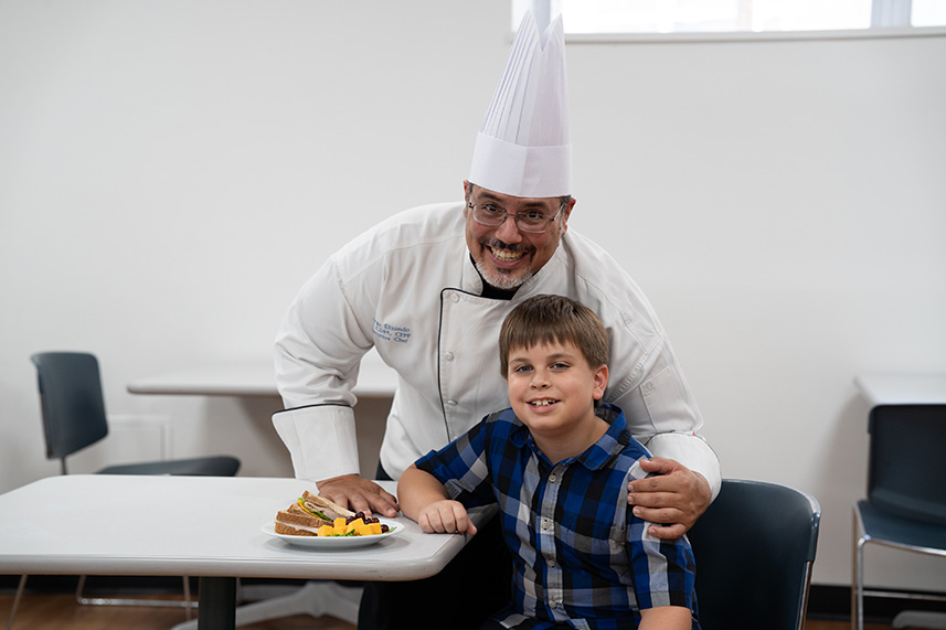 Driscoll Childrens Hospital cafeteria chef with a boy at the table with a healthy lunch.